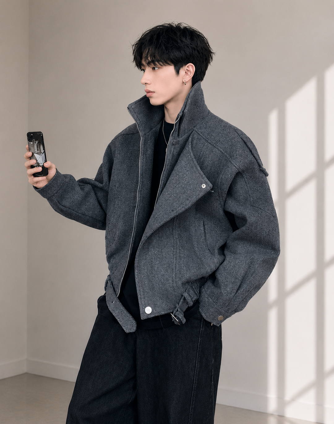 スマホを持つ男性のミドルショット。ワイドなブラックデニムとブルゾンのショート丈が織りなす、今っぽいAラインのバランス感が伝わる一枚。
