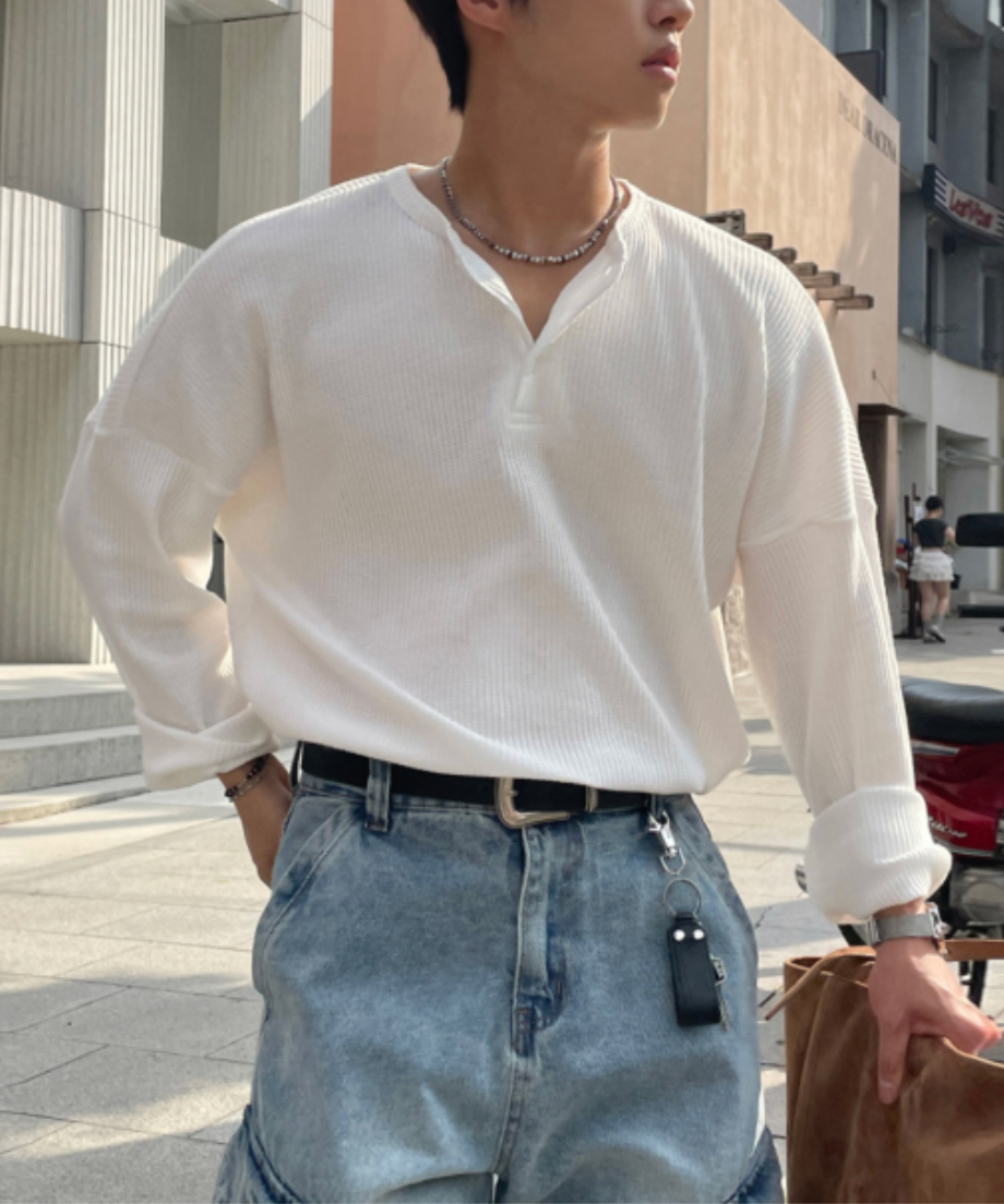 白のワッフル生地の長袖ヘンリーネックTシャツを着用し、ライトブルーのデニムパンツにタックインした男性。