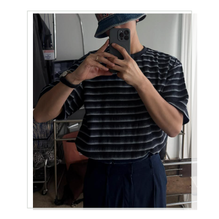ブラックのストライプTシャツとバケットハットを身に纏い、室内の鏡に向かってスマートフォンを構える男性のカット