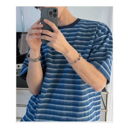 ブルーのストライプTシャツに手をポケットに入れ、手首にブレスレットを覗かせてスマートフォンを持つ男性の斜めからのカット