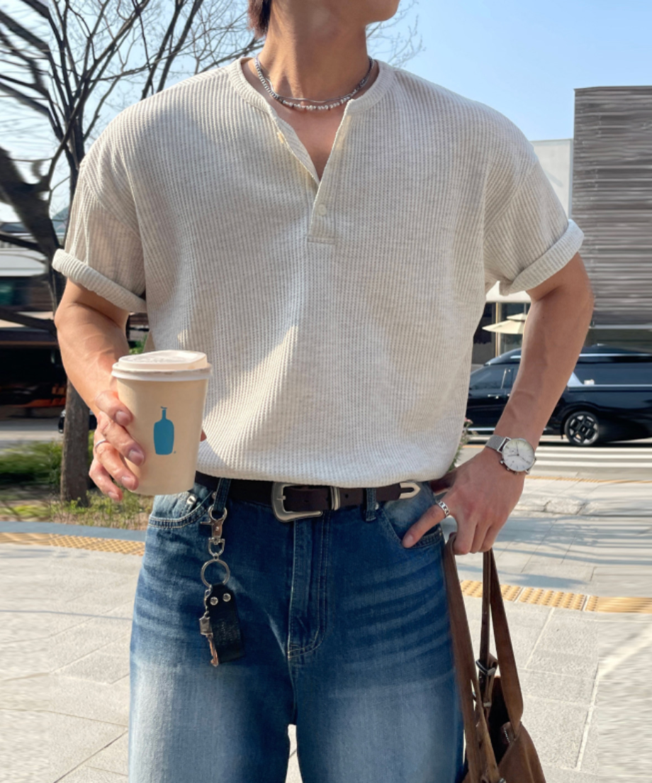 白のワッフル生地の長袖ヘンリーネックTシャツを着用し、ライトブルーのデニムパンツにタックインした男性