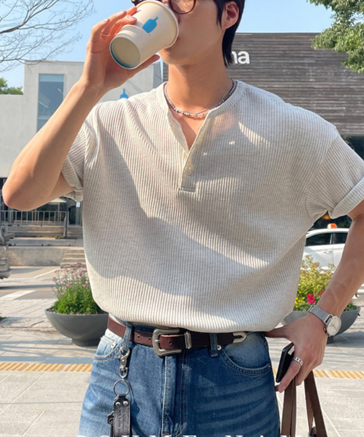 白のワッフル生地の長袖ヘンリーネックTシャツを着用し、コーヒーを飲んでいるカット。