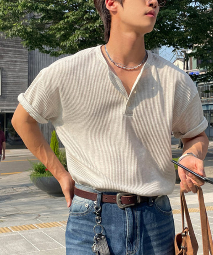 白のワッフル生地の長袖ヘンリーネックTシャツを着用し、ライトブルーのデニムパンツにタックインした男性が横を向いているカット。