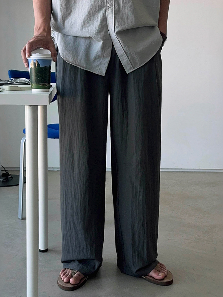 ダークグレーのワイドタックパンツのドレープ感と、足元のサンダルが引き立つ正面からのアップカット