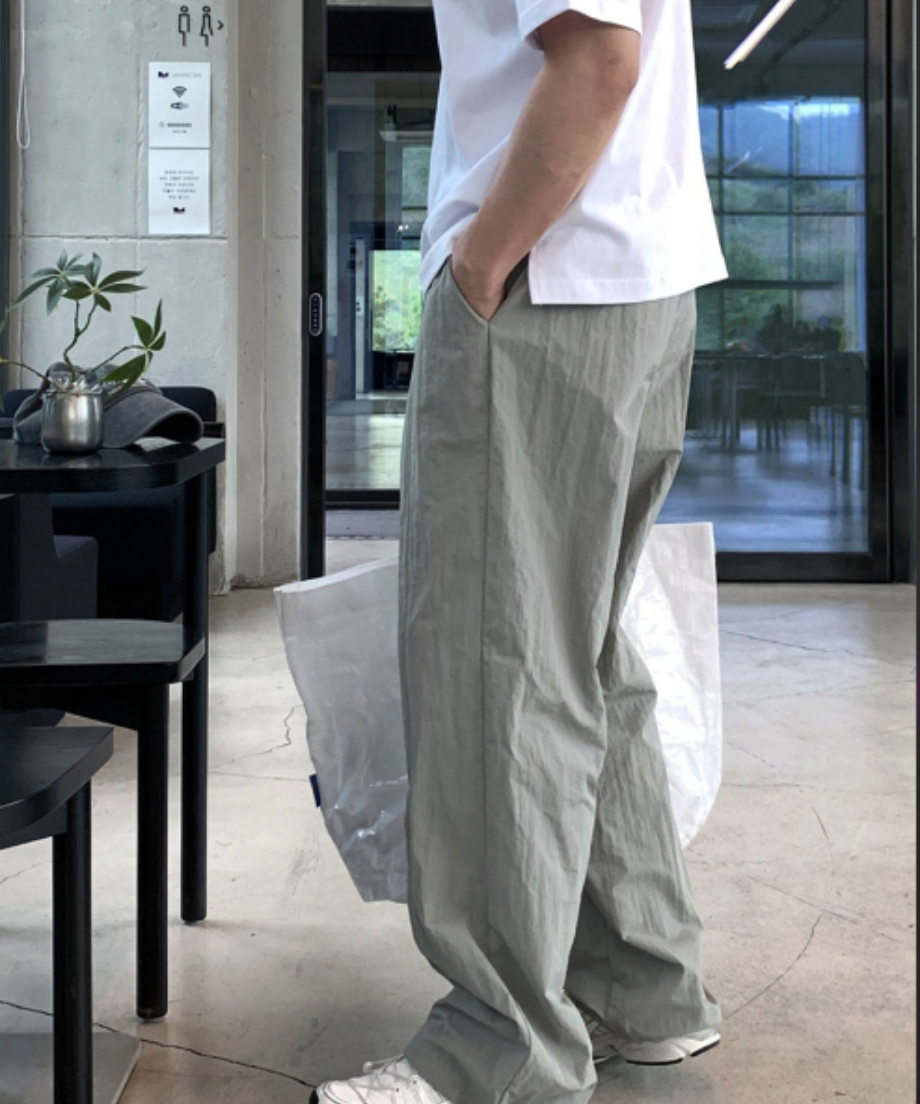 白のTシャツにライトカーキのワイドナイロンパンツを合わせた男性の横向きの着用写真。