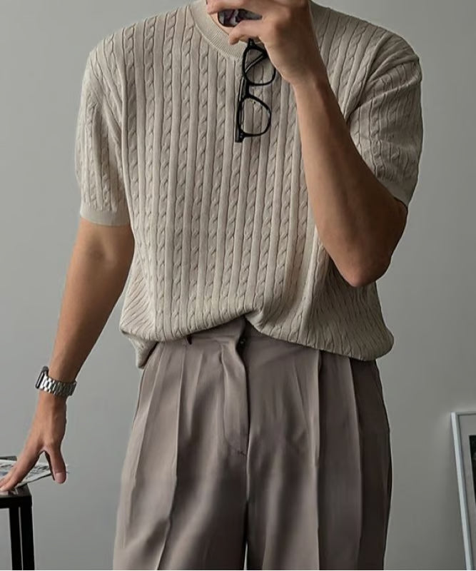 カーキの半袖ケーブルニットを着用し、眼鏡を首元にかけた男性のアップ写真