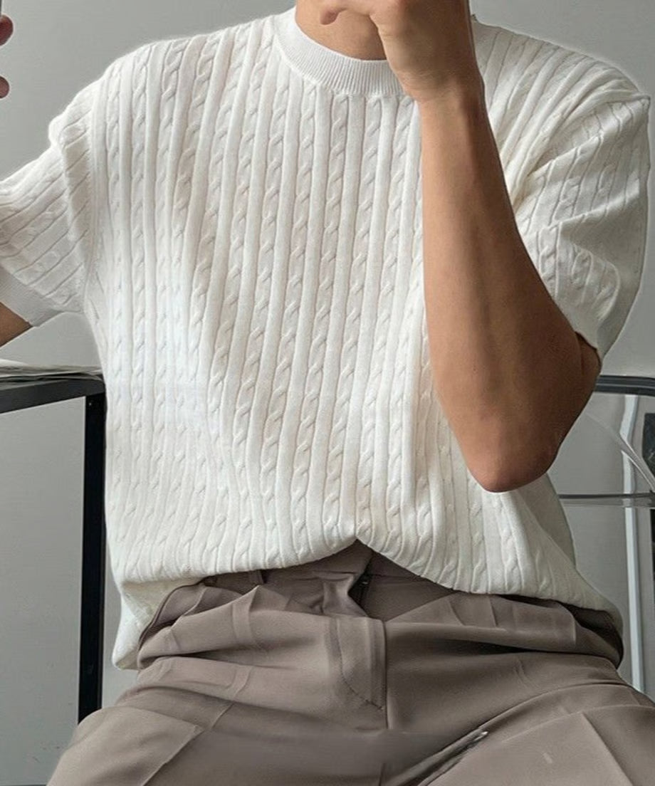 ホワイトの半袖ケーブルニットを着用し、椅子に座る男性の斜め前からのアップ写真