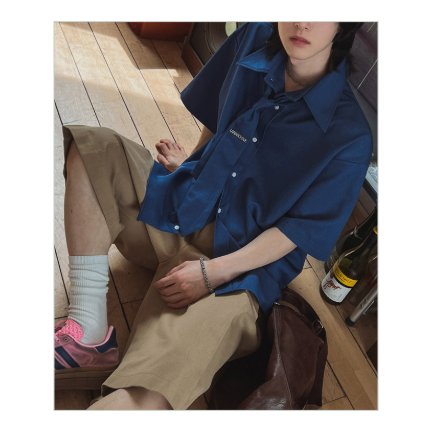 ダークブルーの半袖シャツにベージュのハーフパンツ、ピンクのスニーカーを合わせ、床に座り込む男性のハイアングルカット