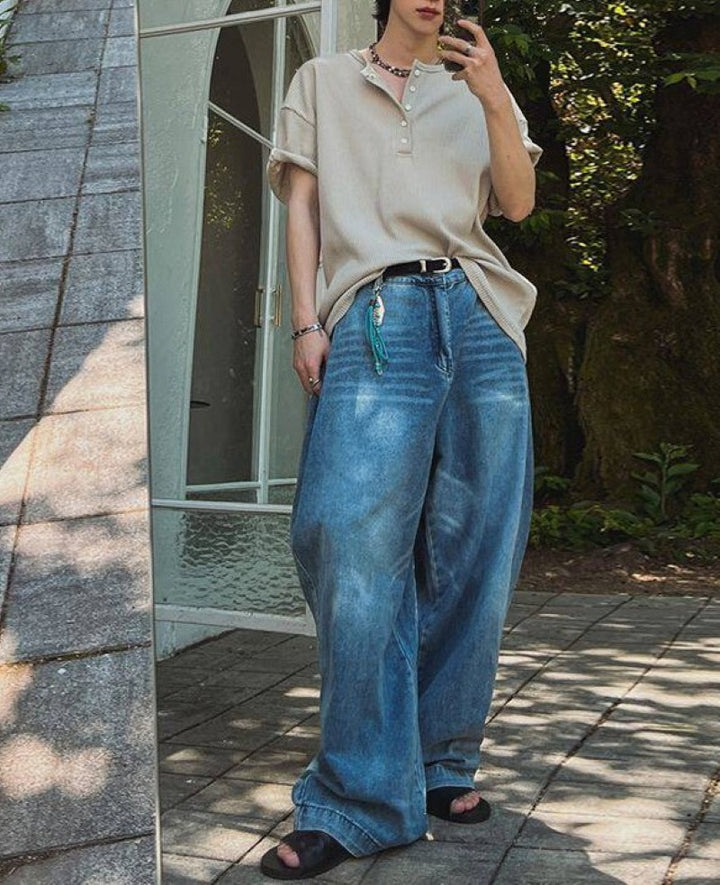 カーキのヘンリーネックワッフルTシャツに、ルーズなワイドデニムと黒のサンダルを合わせた人物の全身鏡越しスタイリング写真。