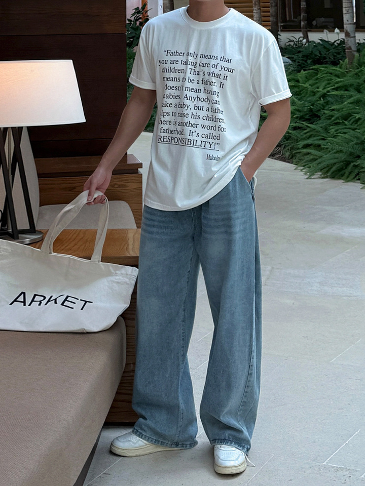 白の英語プリントTシャツとライトブルーのワイドデニムパンツ、白いスニーカーを合わせた男性の全身コーディネート写真。