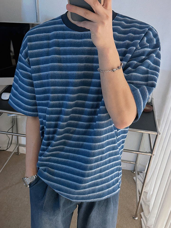 ブルーとライトブルーのストライプTシャツを着用し、メタルブレスレットをつけてスマートフォンを見る男性のアップカット