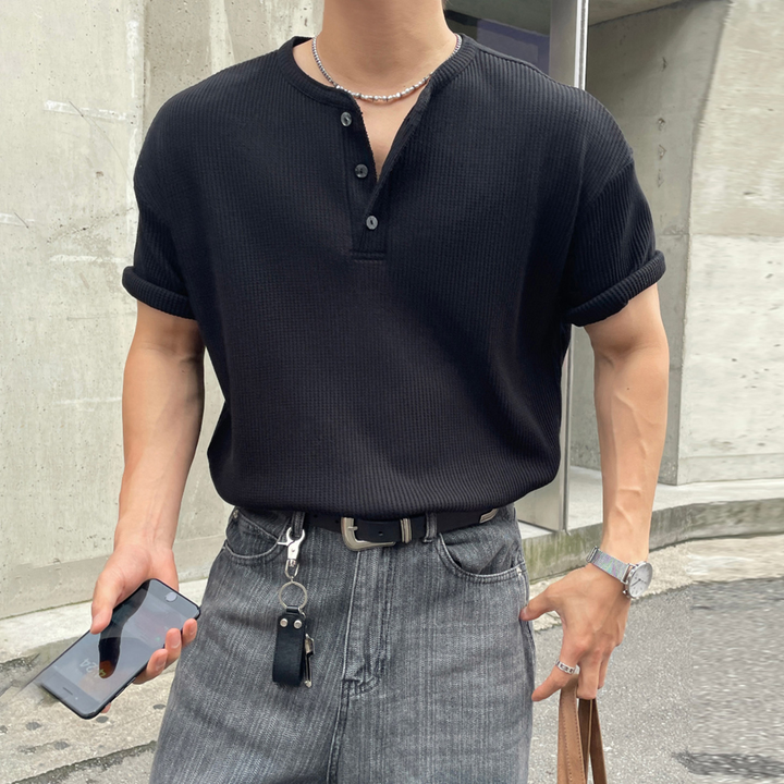 黒のワッフル生地の半袖ヘンリーネックTシャツを着用し、グレーのデニムパンツにタックインした男性のスタイリング
