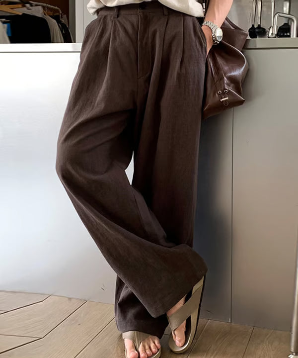 ブラウンのプリーツワイドパンツのポケットに手を入れて立つ男性の斜めからのアップ写真