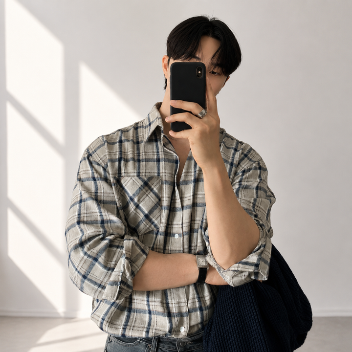 ベージュのチェック柄シャツのボタンを少し開け、片手でスマートフォンを持って撮影する男性のチェストアップ。