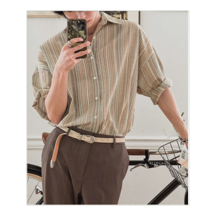 カーキストライプ半袖シャツを着用し、自転車の前に立つ男性がスマホを見ているスタイリッシュなカット