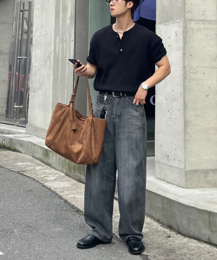 黒のワッフル半袖ヘンリーネックTシャツとグレーのワイドデニムを着用し、ブラウンのトートバッグを片手に歩く男性の全身スタイリング
