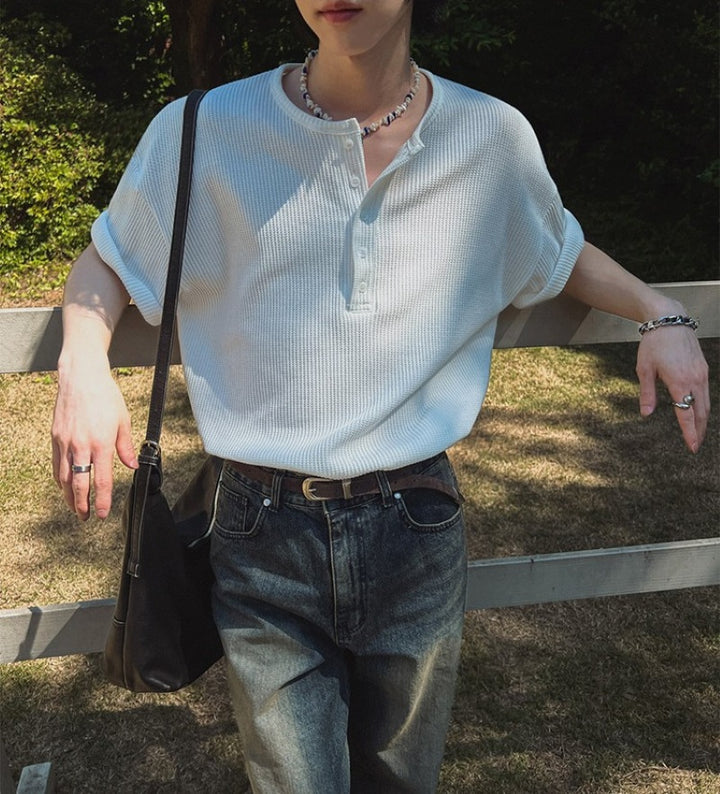 ホワイトのヘンリーネックワッフルTシャツを着用し、両腕を柵に預けて正面を向いている人物のスタイリング写真。