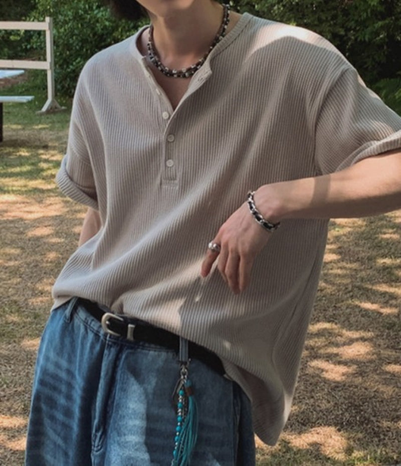 カーキのヘンリーネックワッフルTシャツを着用し、ネックレスやブレスレットを身につけた人物の斜め前からのアップ写真。