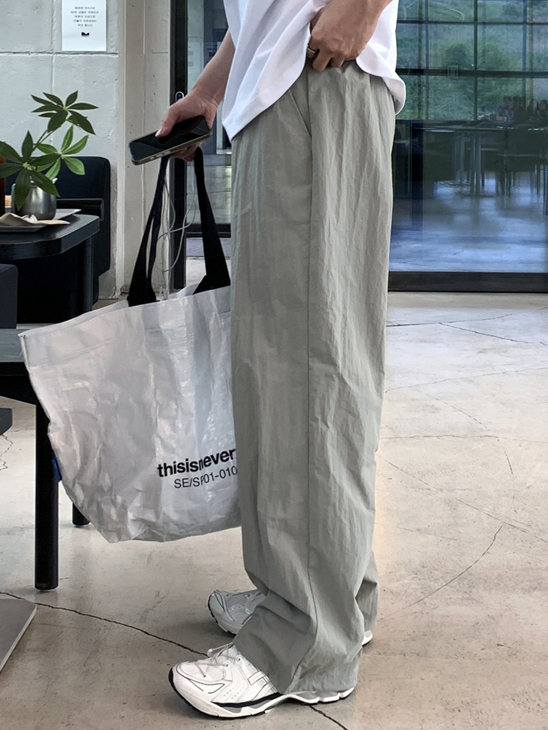 白いTシャツにライトカーキのワイドストレートパンツ、白いスニーカーを合わせ、白いショッパーバッグを持った男性の立ち姿。