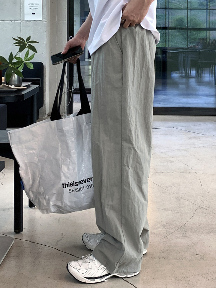 白いTシャツにライトカーキのワイドストレートパンツ、白いスニーカーを合わせ、白いショッパーバッグを持った男性の立ち姿。
