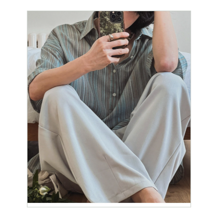ストライプ半袖シャツにライトグレーのワイドパンツを合わせた男性が床に座った正面ショット。