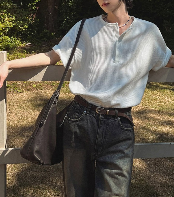 ホワイトのヘンリーネックワッフルTシャツを着用し、黒のショルダーバッグとデニムを合わせた人物の屋外スナップ写真。
