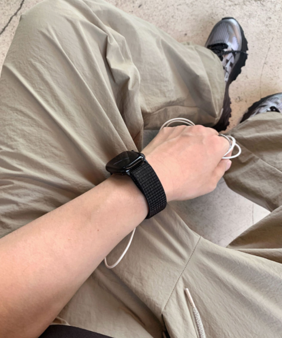 ベージュのナイロンパンツを履いて座り、腕に黒のスマートウォッチを着用した男性の手元のアップ写真。