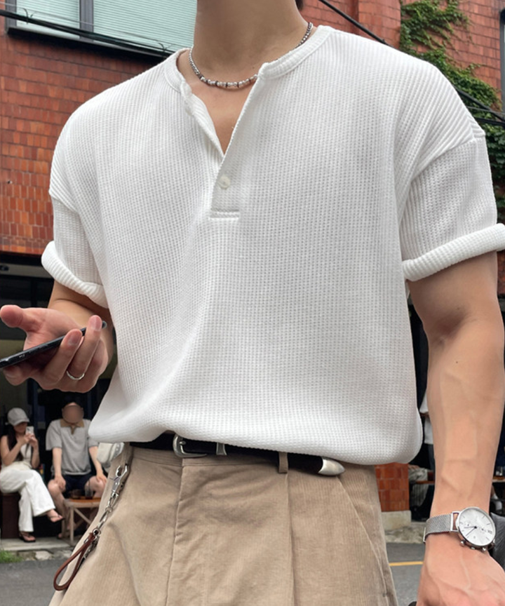 白のワッフル生地の半袖ヘンリーネックTシャツを着用し、ベージュのタックパンツにタックインした男性のアップ