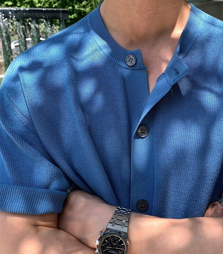 ブルーのバンドカラー半袖ニットカーディガンを着用し、腕組みをしている男性の胸元のアップ写真。
