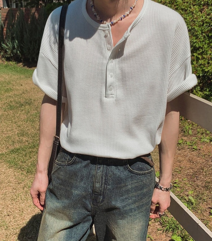 ホワイトのヘンリーネックワッフルTシャツを着用し、首元にウッドビーズ調のネックレスを身につけた人物の屋外スナップ写真。