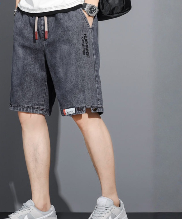 グレーのデニムハーフパンツと白いTシャツ、グレーのスニーカーを着用した男性の、斜め前方からの全身コーディネート写真。