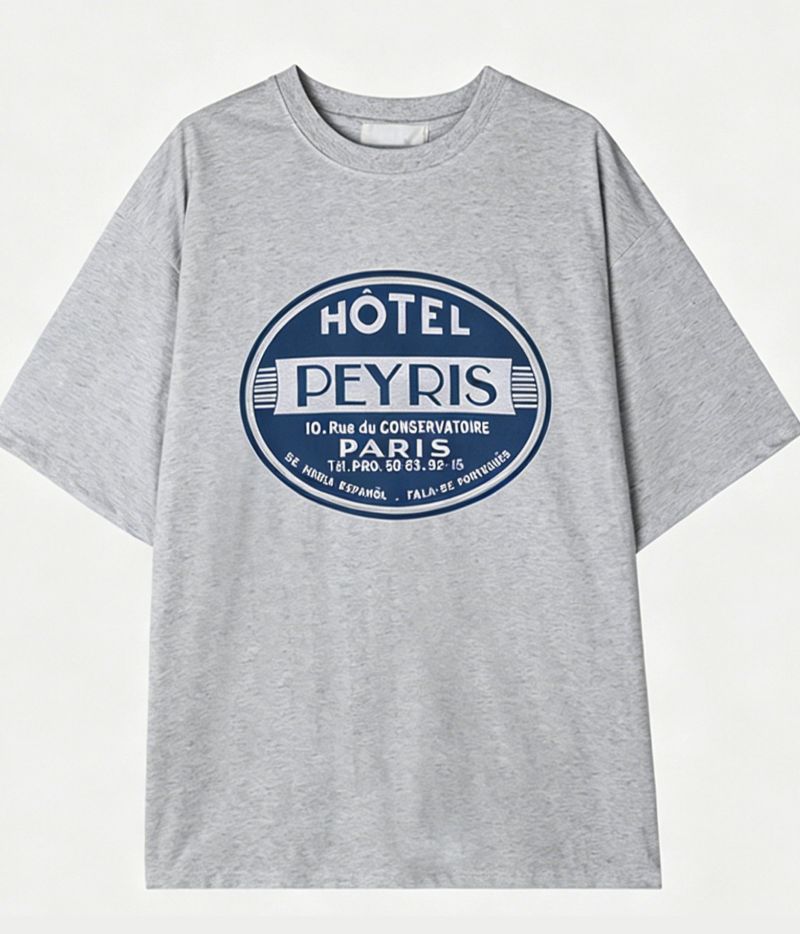 白を基調とした背景に、綺麗に配置されたライトグレーのグラフィックTシャツの平置き正面カット。フロント中央のクラシカルなサークルロゴデザインがはっきりと見えます。
