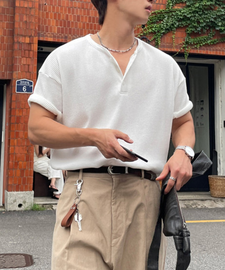 白のワッフル半袖ヘンリーネックTシャツとベージュのワイドデニムを着用し、ブラックのトートバッグを片手に歩く男性の全身スタイリング