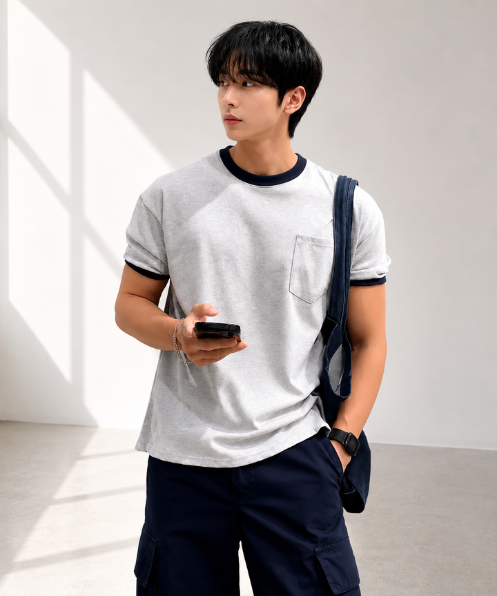 ライトグレーにネイビーのリブが映えるリンガーポケットTシャツを着用し、片手をポケットに入れながらスマートフォンを操作する男性のフロントカット。