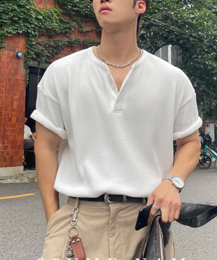白の半袖ヘンリーネックTシャツにベージュのチノパンツを合わせ、黒のレザーバッグを手にした男性の正面カット。