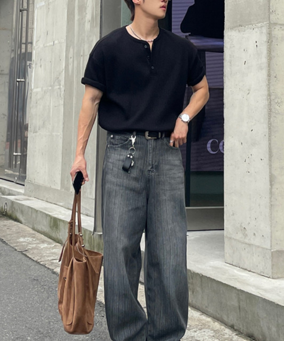 黒のワッフル半袖ヘンリーネックTシャツを着用し、ポケットに手を入れて佇む男性の全身カット。
