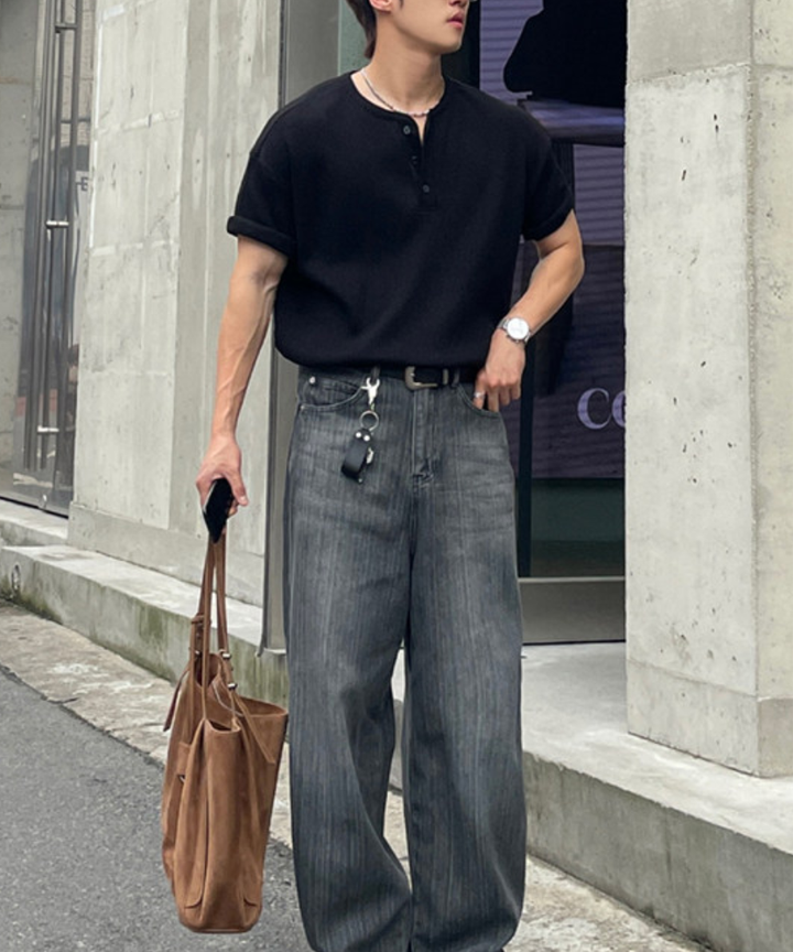 黒のワッフル半袖ヘンリーネックTシャツを着用し、ポケットに手を入れて佇む男性の全身カット。