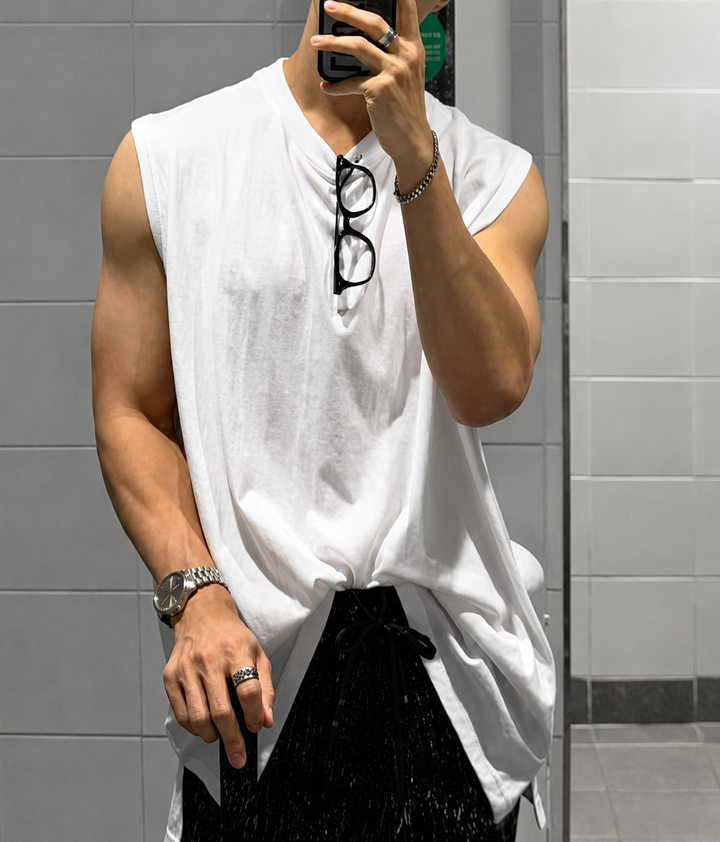 ホワイトのマッスルタンクTシャツを着用し、鏡越しにスマートフォンで自撮りをする男性の全身カット。胸元に眼鏡を掛け、黒のハーフパンツを合わせています。