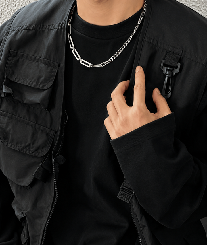 黒のTシャツとベストを着用した男性が胸元に手を添えるカットで、首元のコンビネックレス幅広のメタルリングが連動したストリート感溢れるカット