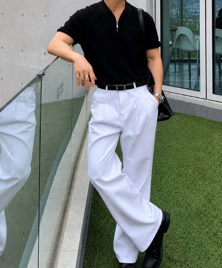 ブラックのハーフジップニットに白いワイドパンツ、黒の革靴を合わせ、ガラスの手すりに寄りかかるスタイリッシュな全身コーディネートカット。