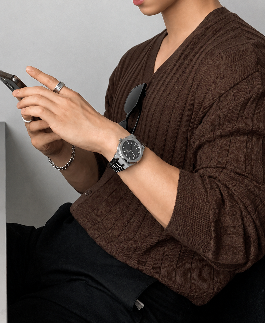ブラウンのリブカーディガンを着用し、両手でスマートフォンを操作している男性のクローズアップカット。