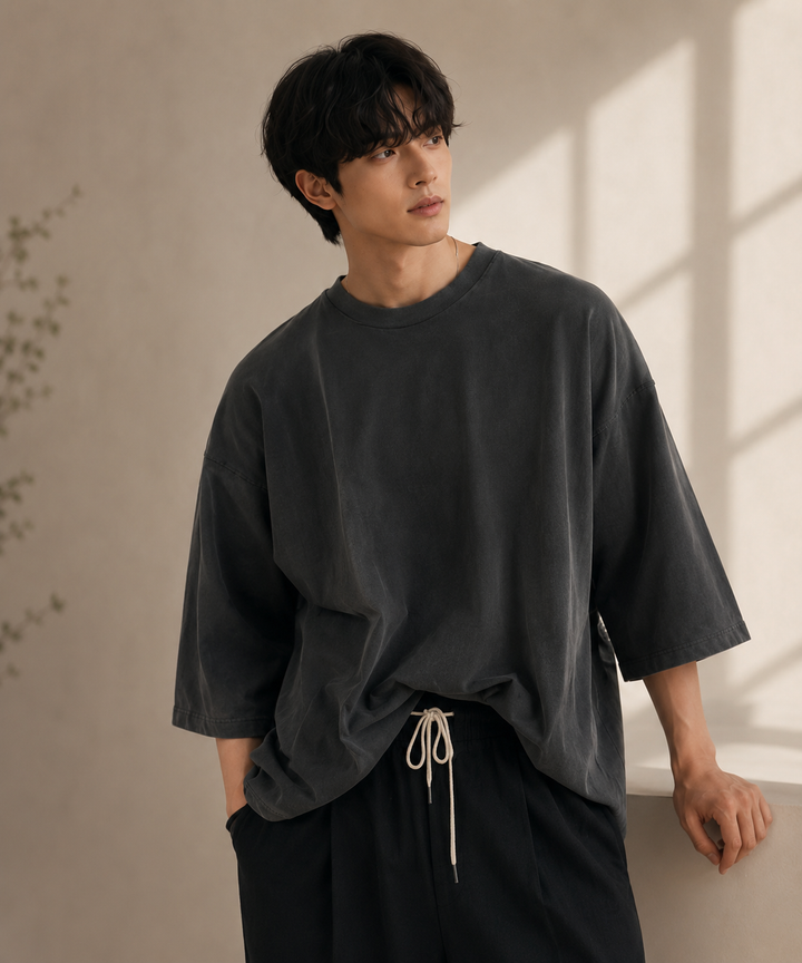 アイアングレーのオーバーサイズTシャツに、白いドローコードがついた黒のイージーパンツを合わせた男性の上半身ショット。