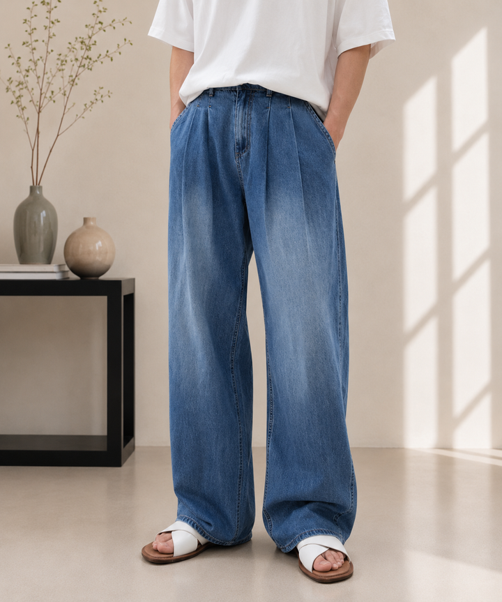 ブルーのタック入りワイドデニムパンツに、白の半袖Tシャツをタックインし、白いクロスストラップサンダルを合わせた男性。