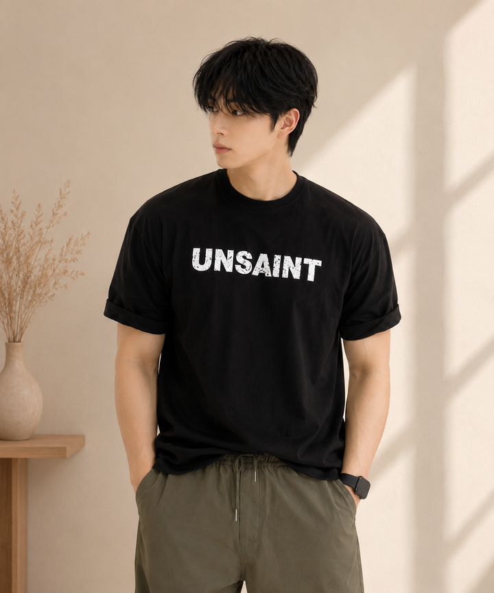 ブラックの「UNSAINT」ロゴTシャツとオリーブのドローコード付きナイロンショーツを着用した男性の写真。