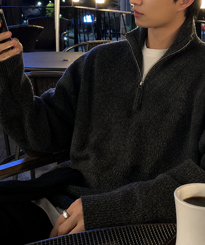 夜のテラス席で、アイアングレーのハーフジップニットを着用し、手元に白いコーヒーカップを置いて横を向いている男性のシックな雰囲気のカット。