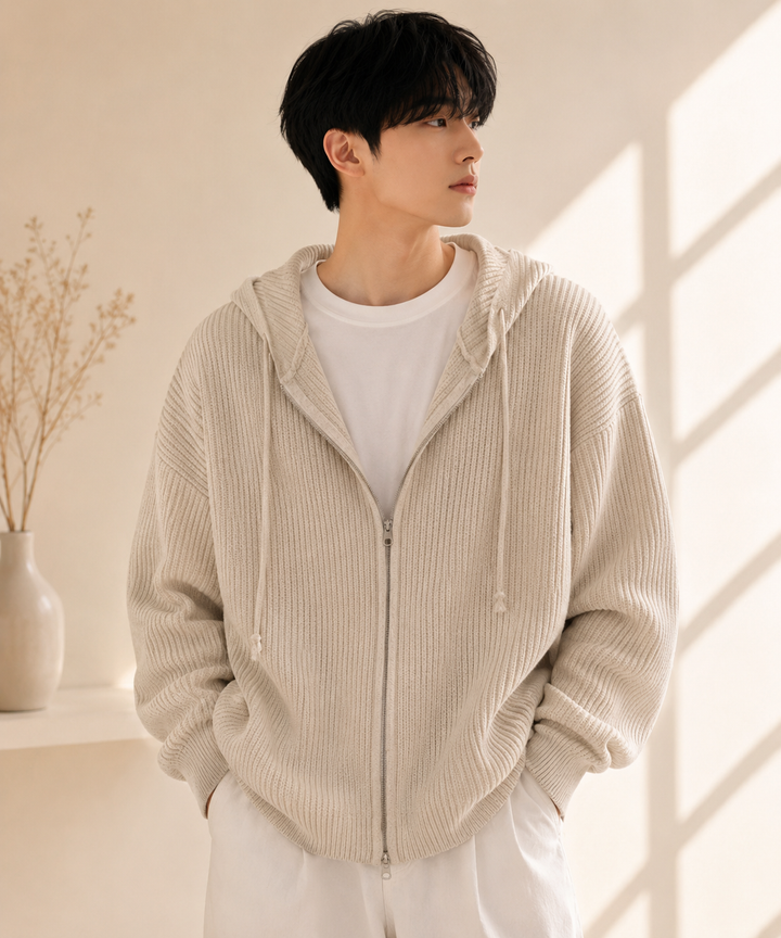 ベージュのリブ編みジップアップニットパーカーに白のTシャツと白のパンツを合わせた男性。


