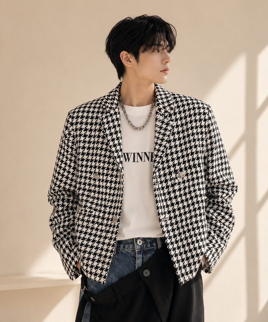 チェック柄のショートジャケットを着用し、インナーの白Tシャツにシルバーの太めチェーンネックレスを合わせた男性の正面アップカット。アシメトリーな黒のボトムスを合わせています。