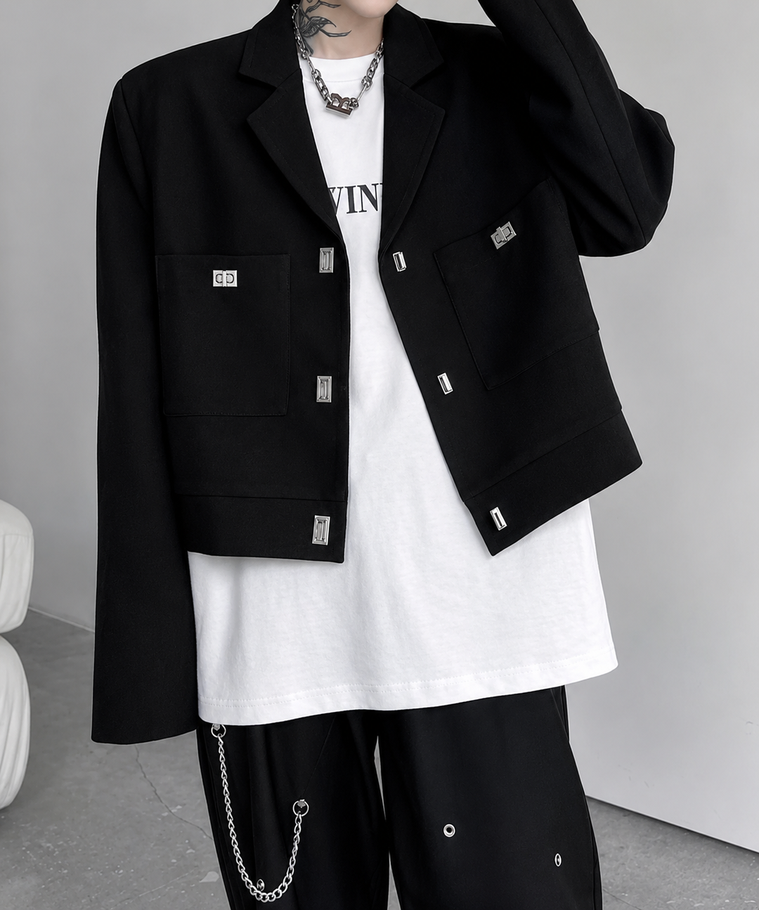 スクエア型のメタルバックルが際立つブラックのショートジャケットに、白のTシャツと黒のワイドパンツ、ウォレットチェーンを合わせたスタイリッシュな正面カット。