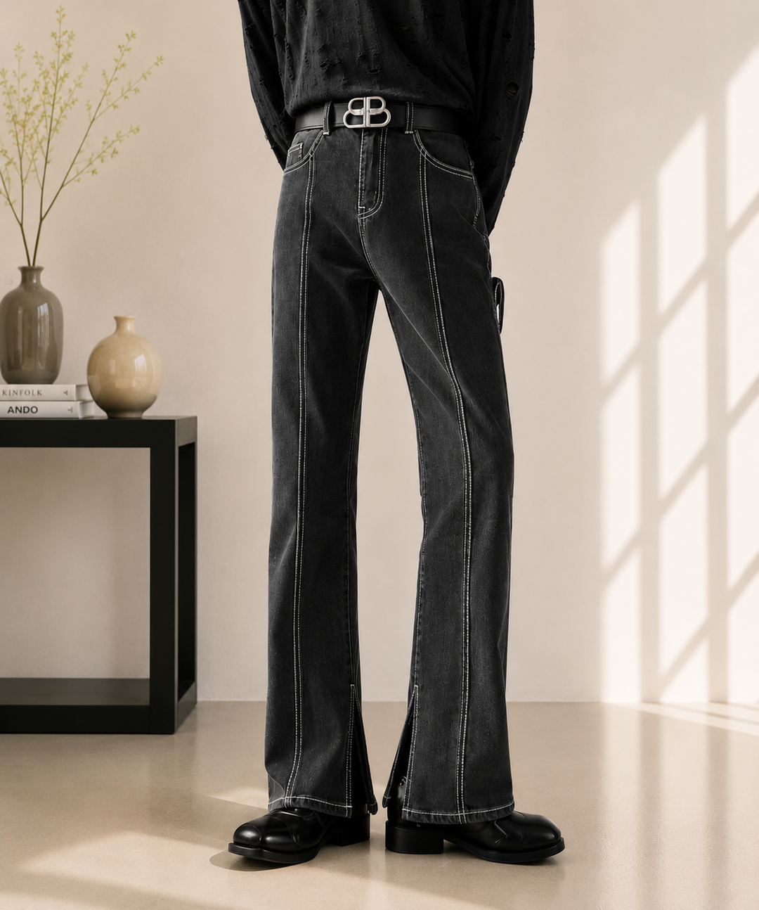 センターシームと裾スリットが特徴のブラックフレアデニムパンツを着用した男性の全体正面。ベルトを着用。