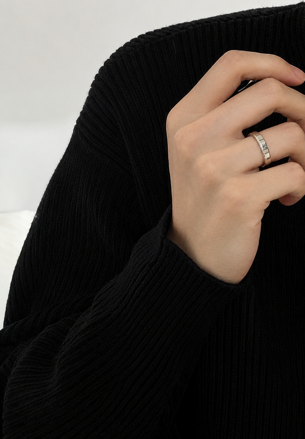 黒のニットを着用した男性が、格子柄のオープンリングをしている手元のスタイリングカット。